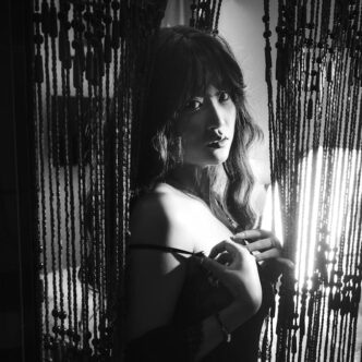 Dramática fotografía en blanco y negro de una mujer detrás de cortinas de cuentas.