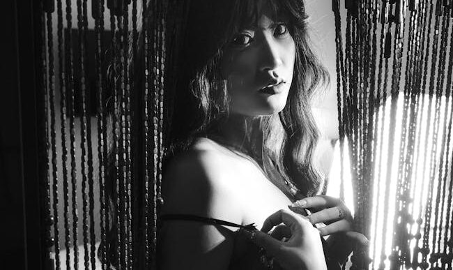 Dramática fotografía en blanco y negro de una mujer detrás de cortinas de cuentas.