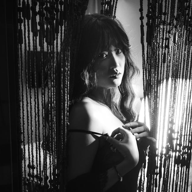 Dramática fotografía en blanco y negro de una mujer detrás de cortinas de cuentas.