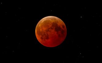 Esta cautivadora imagen captura una luna de sangre durante un eclipse lunar total contra un cielo nocturno estrellado.