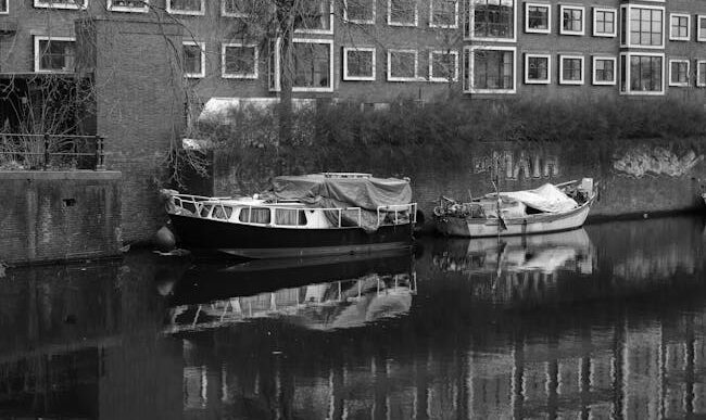 Fotografía en blanco y negro de barcos amarrados a lo largo de un canal con arquitectura de Ámsterdam.