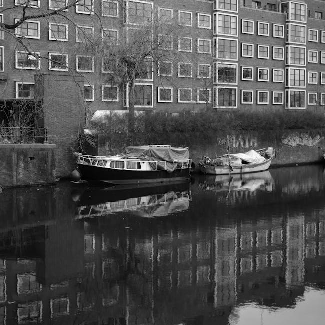 Fotografía en blanco y negro de barcos amarrados a lo largo de un canal con arquitectura de Ámsterdam.
