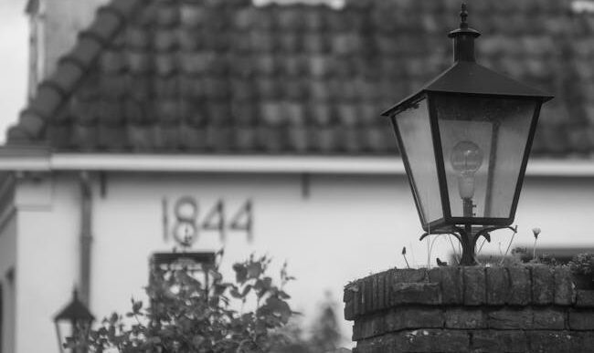 Imagen en blanco y negro de una casa de ladrillo vintage y un poste de luz exterior.