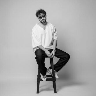 Retrato en blanco y negro de un hombre con gafas de sol, posando elegantemente en un estudio de Teherán.