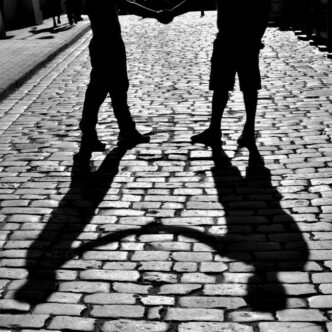 Silueta de dos personas dándose la mano, proyectando sombras sobre una calle adoquinada en Rzeszów, Polonia.