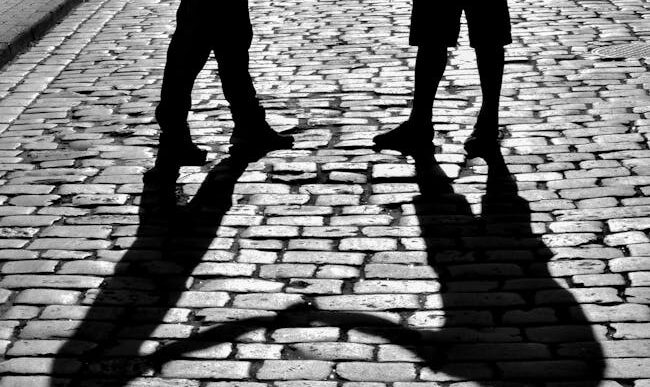 Silueta de dos personas dándose la mano, proyectando sombras sobre una calle adoquinada en Rzeszów, Polonia.